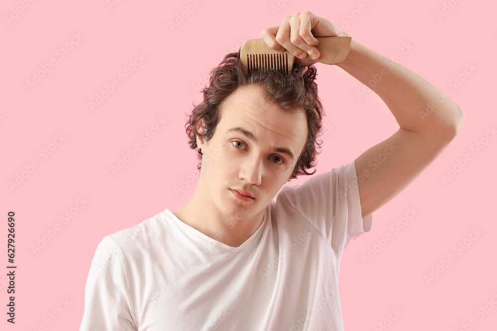 Young man combing hair on pink background