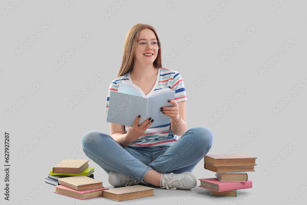 Teenage girl with books sitting on light background