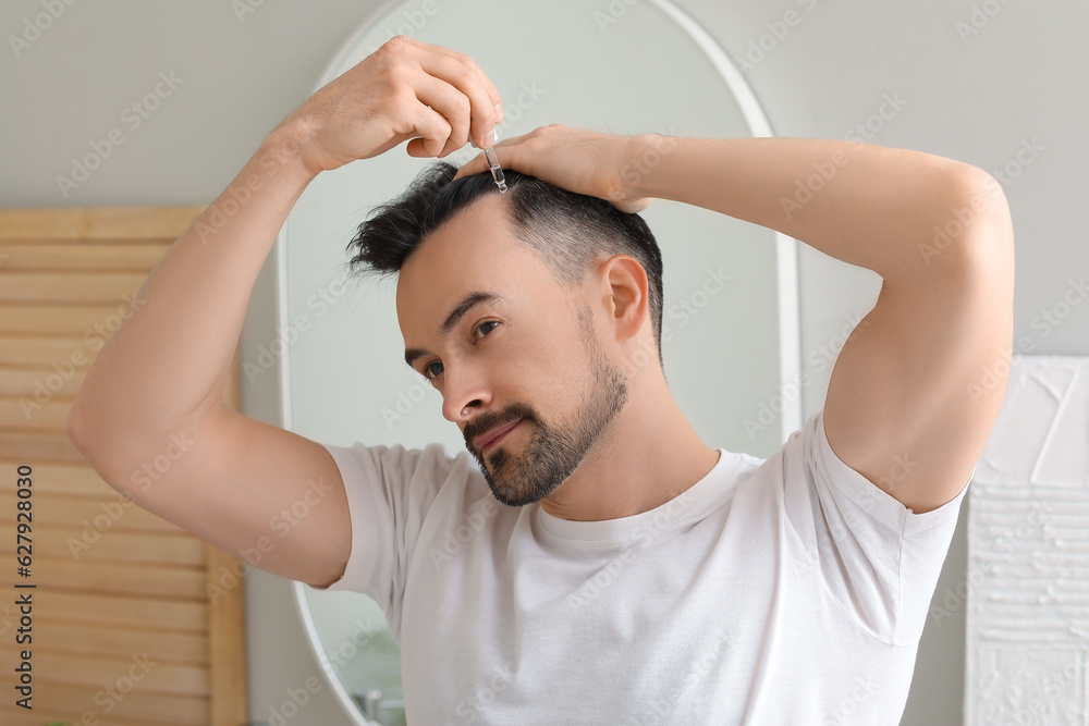 Handsome man using serum for hair growth in bathroom