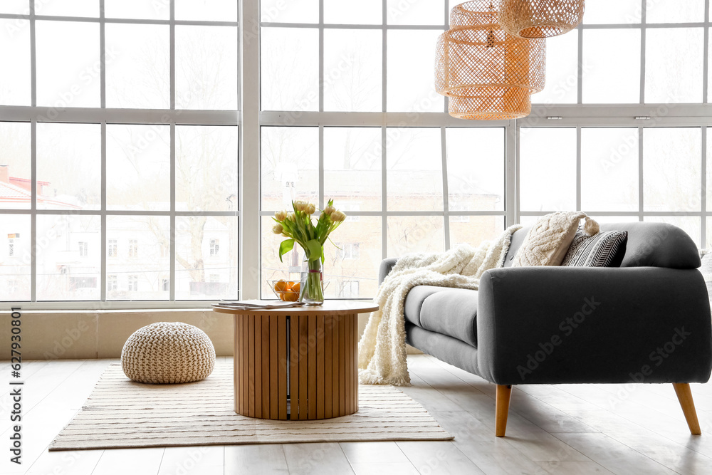 Interior of stylish living room with cozy sofa and coffee table near big window