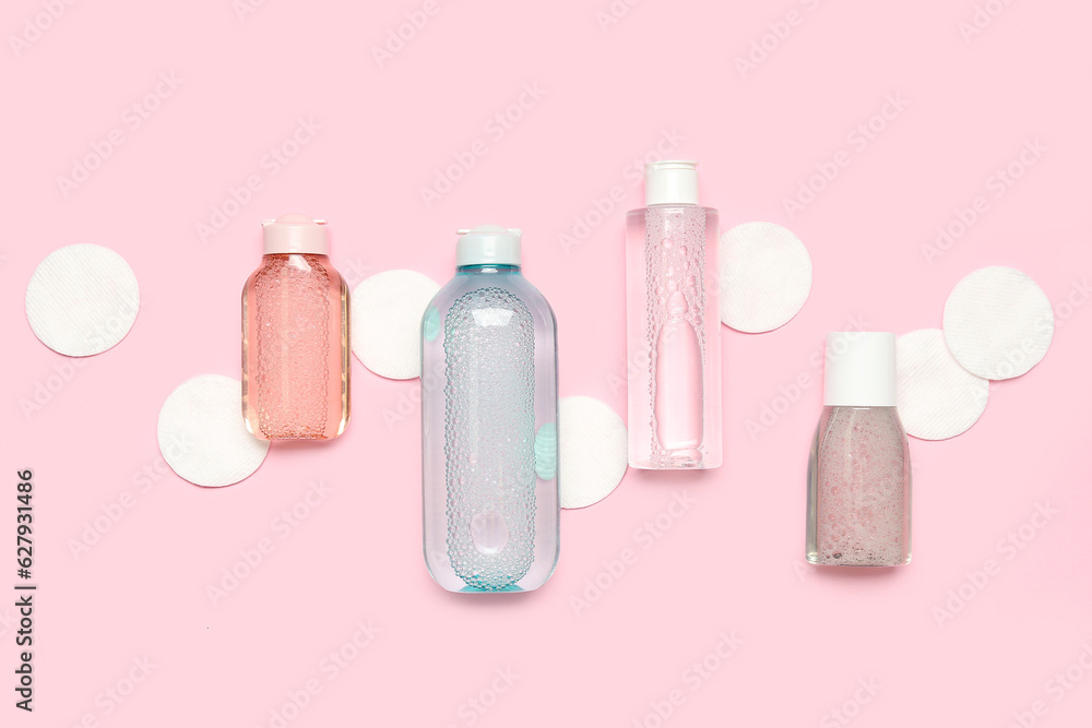 Bottles of micellar water with cotton pads on pink background