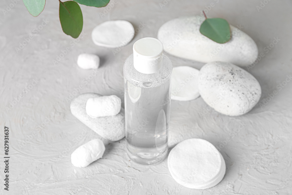 Bottle of micellar water with cotton balls, pads and spa stones on grey table