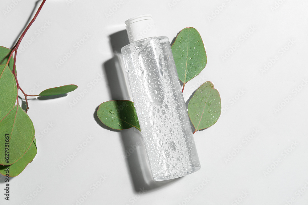 Bottle of micellar water with eucalyptus branches on light background