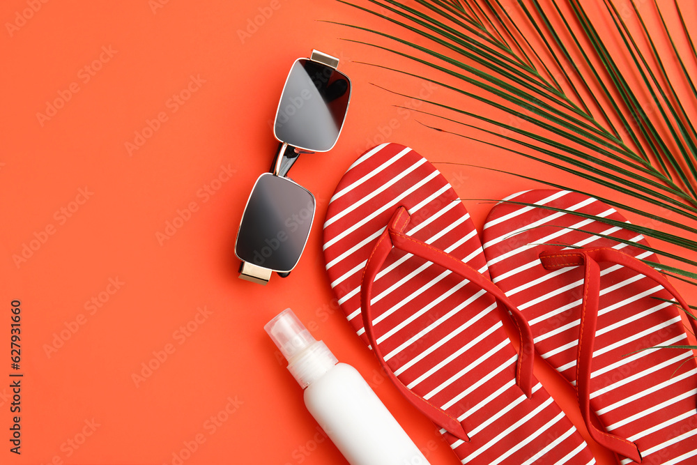 Flip-flops, sunglasses, bottle of sunscreen and palm leaf on red background