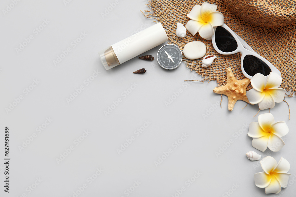 Sunglasses, compass, plumeria flowers and straw hat on grey background