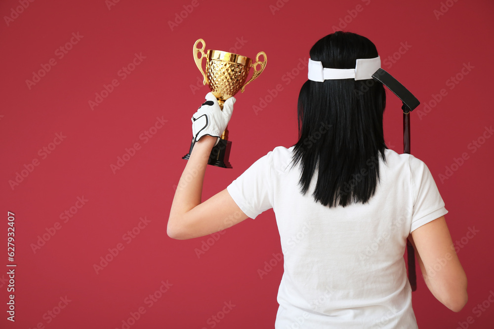 Female golfer with gold cup on red background, back view