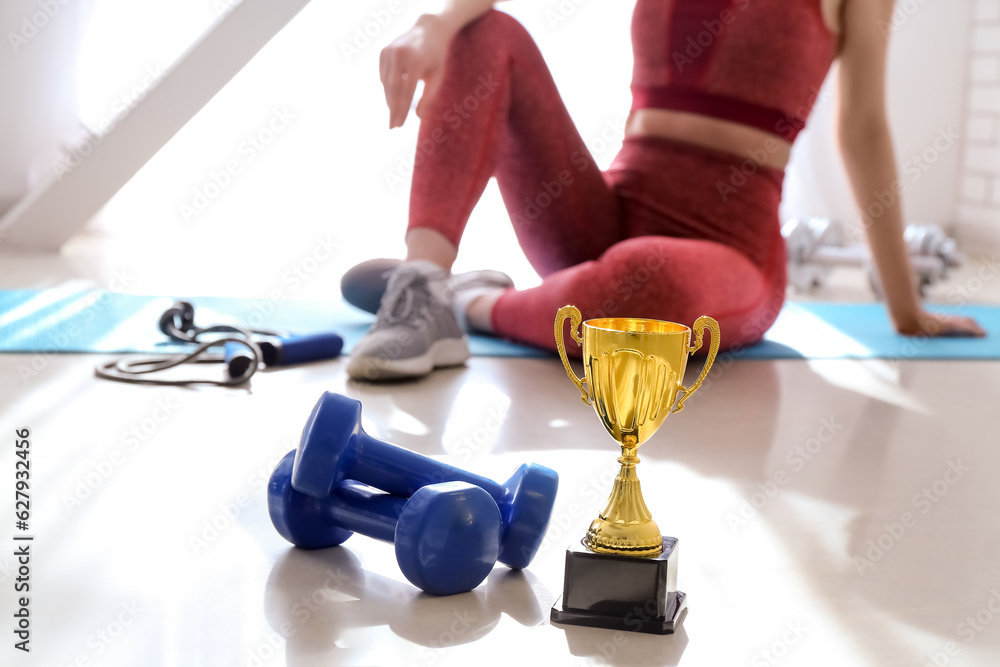 Gold cup with dumbbells on floor in gym, closeup