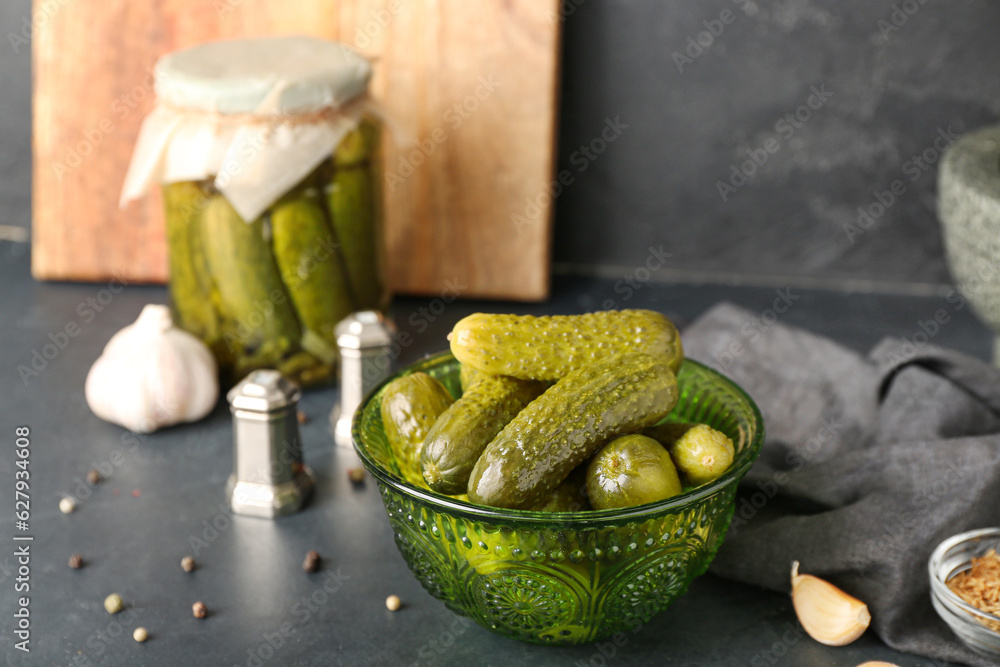 Jar and bowl with tasty canned cucumbers on black table