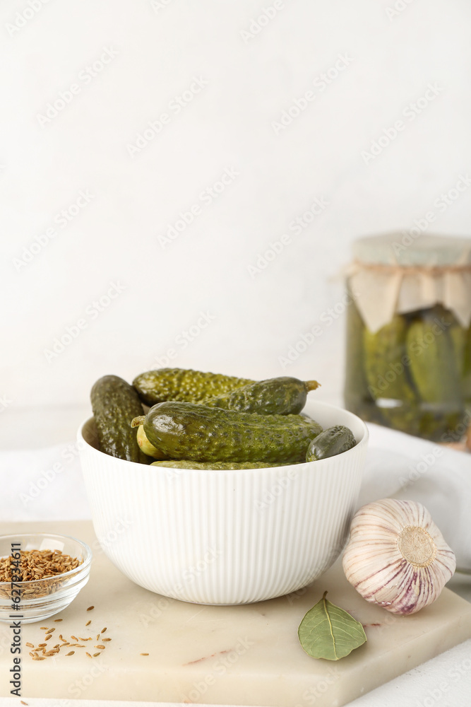 Board with bowl of canned cucumbers and ingredients on white table