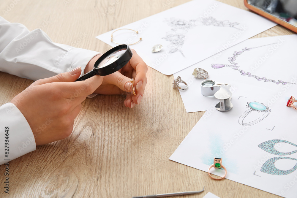 Female jeweler examining ring on wooden table, closeup