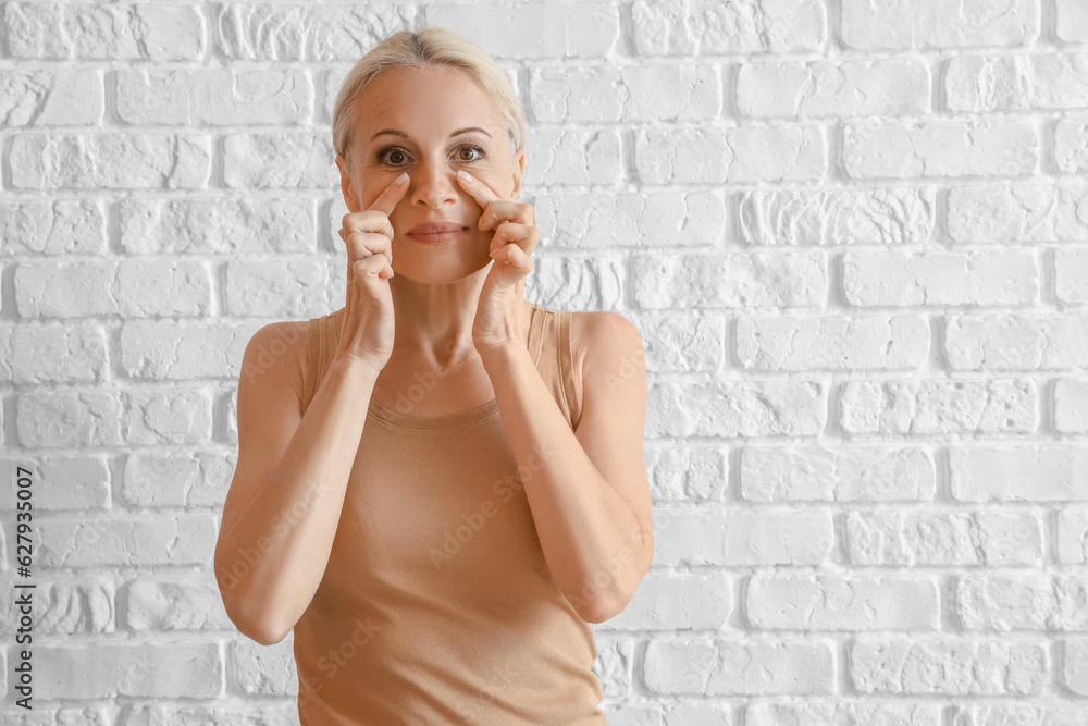 Mature woman doing face building exercise on white brick background