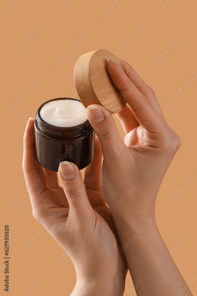 Hands holding cosmetic cream on beige background