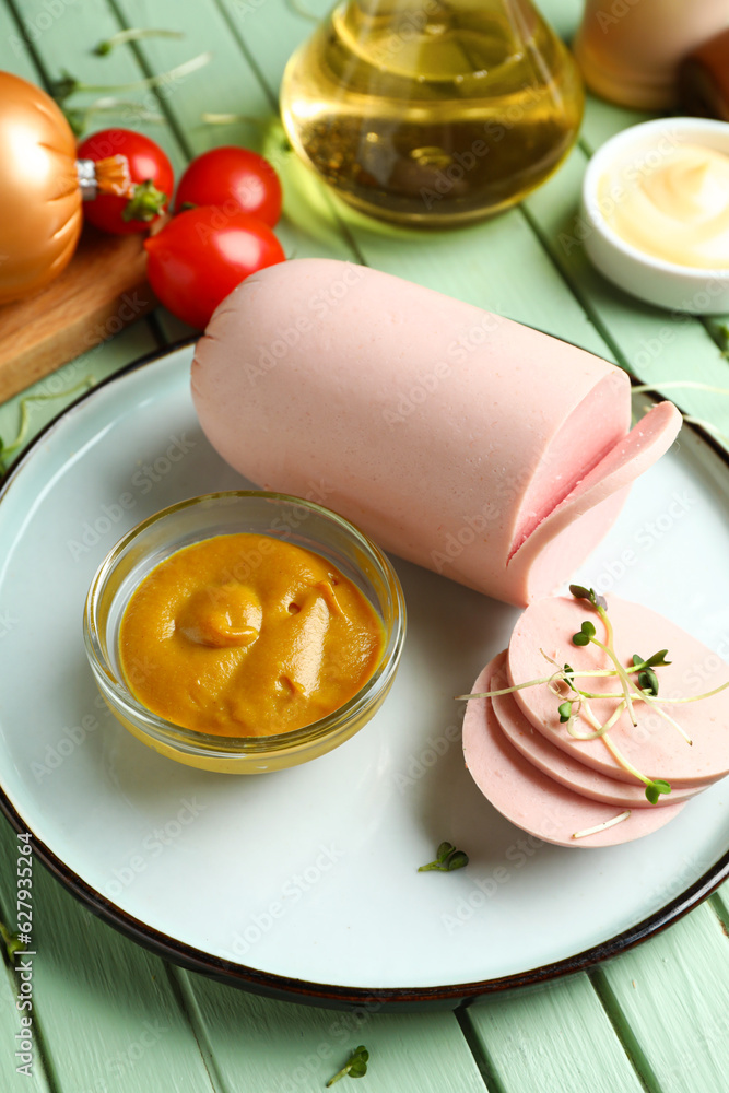 Plate with tasty boiled sausage and sauce on green wooden background