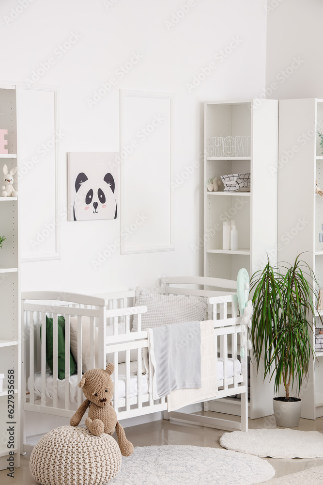 Stylish interior of childrens room in white tones with baby bed and shelving unit