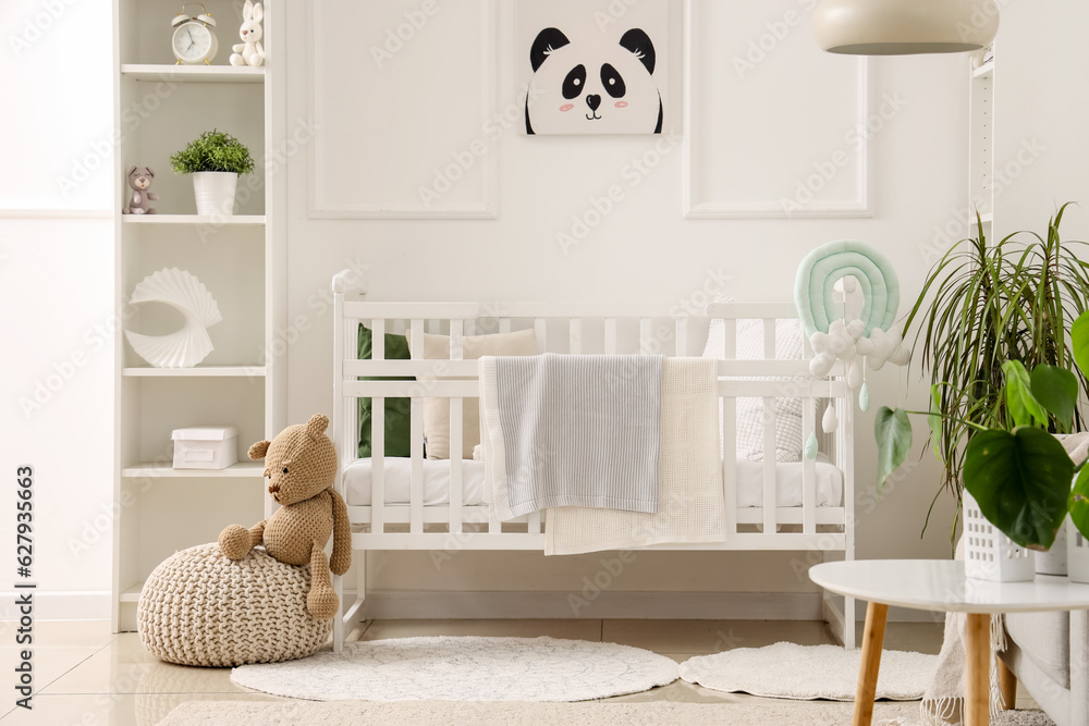 Stylish interior of childrens room in white tones with baby bed and shelving unit