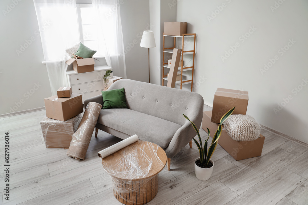 Sofa with rolled carpet and cardboard boxes in living room on moving day