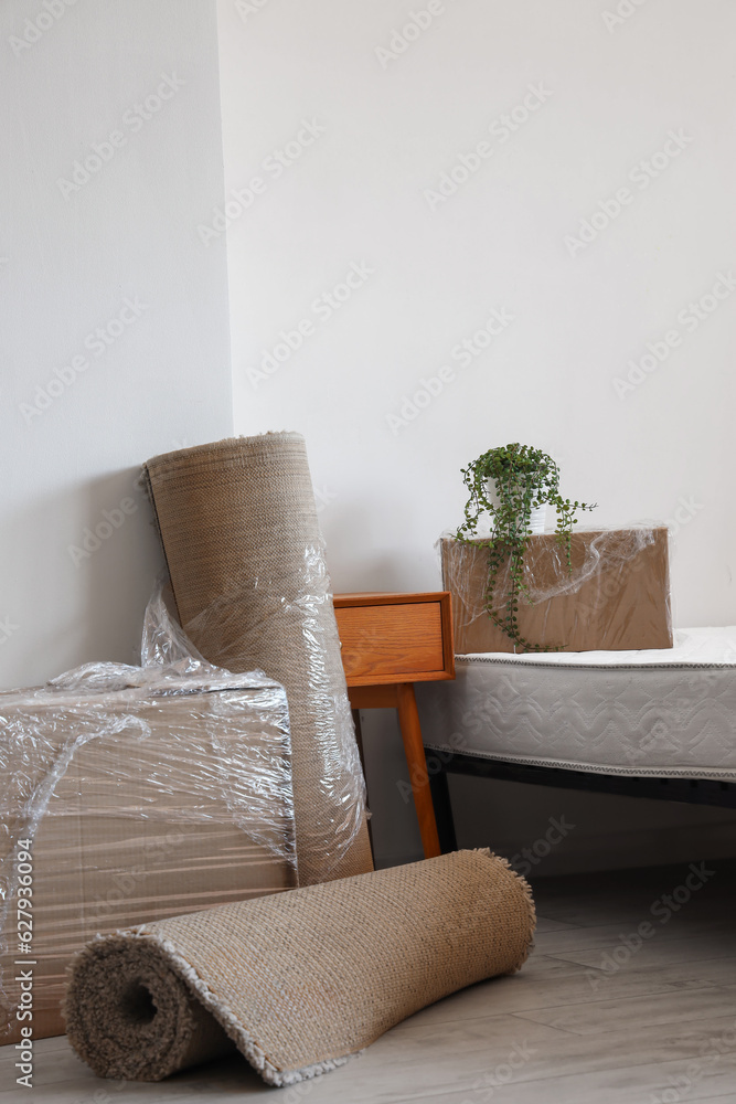 Cardboard boxes with rolled carpets and bed in room on moving day