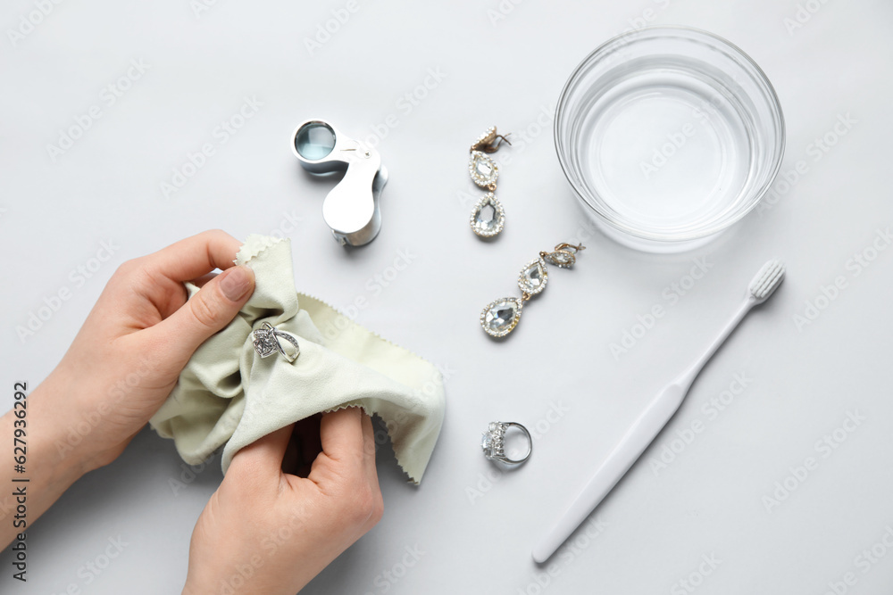 Woman polishing beautiful ring with napkin on white background