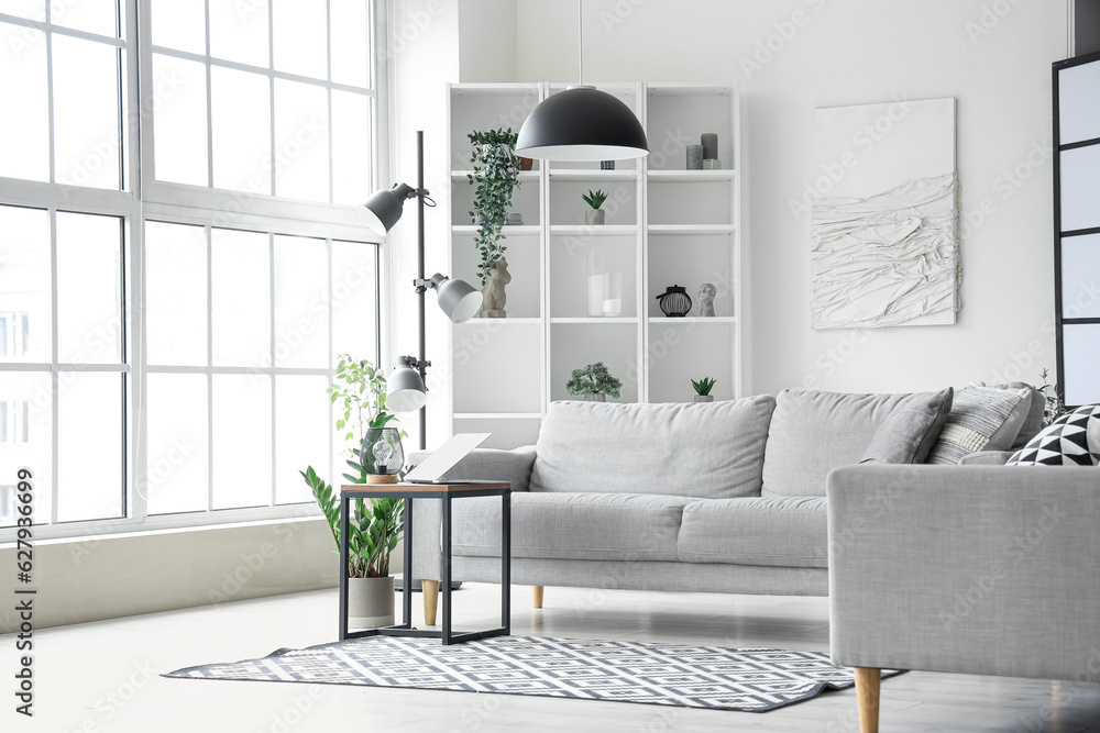 Interior of light living room with cozy grey sofa and modern laptop on coffee table