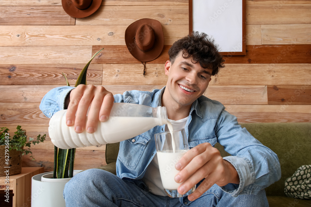 Young man pouring milk into glass at home