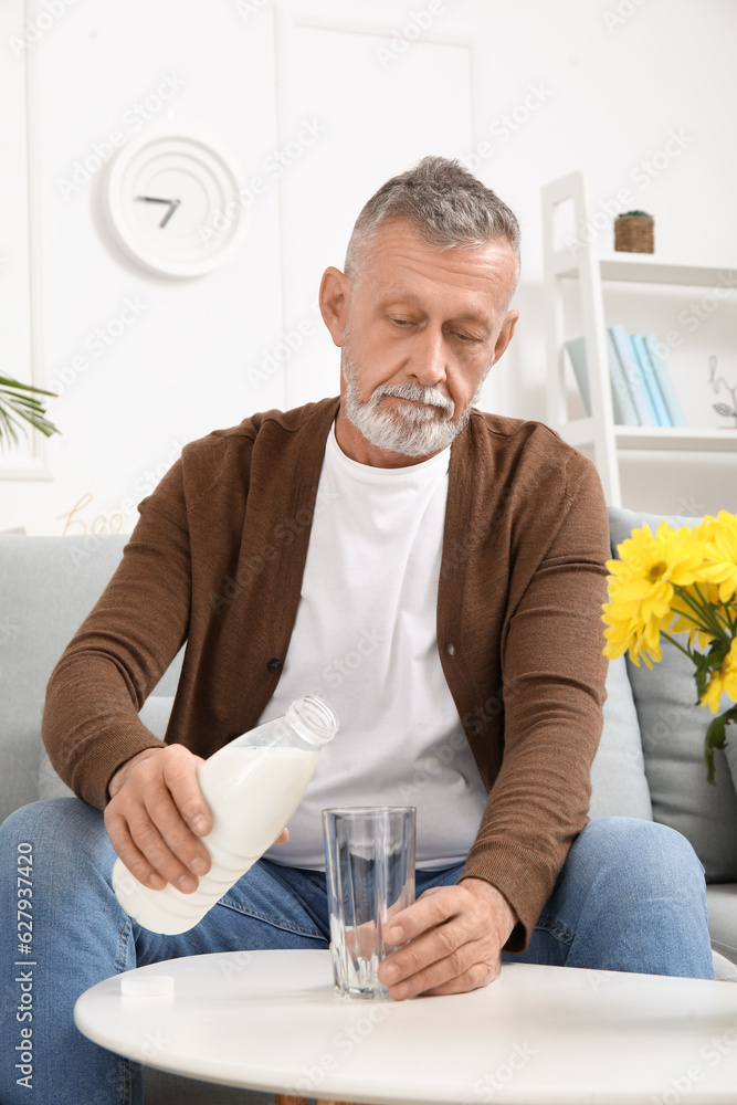 Mature man pouring milk into glass at home