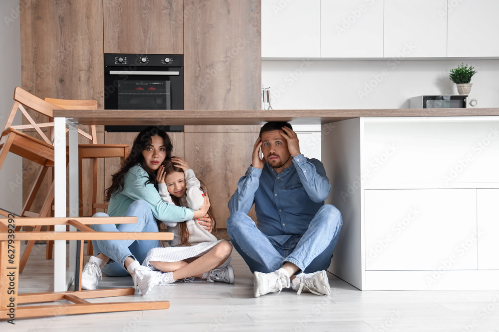 Scared family hiding under dining table during earthquake in kitchen