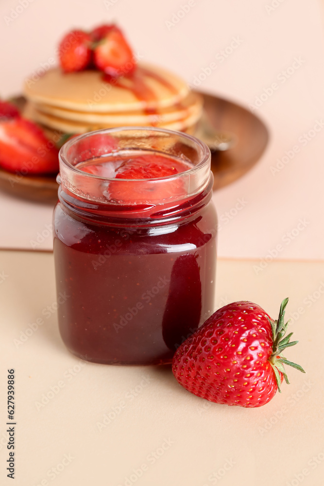 Jar of sweet strawberry jam on beige background