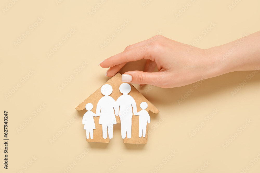 Female hand with figures of family and wooden house on beige background