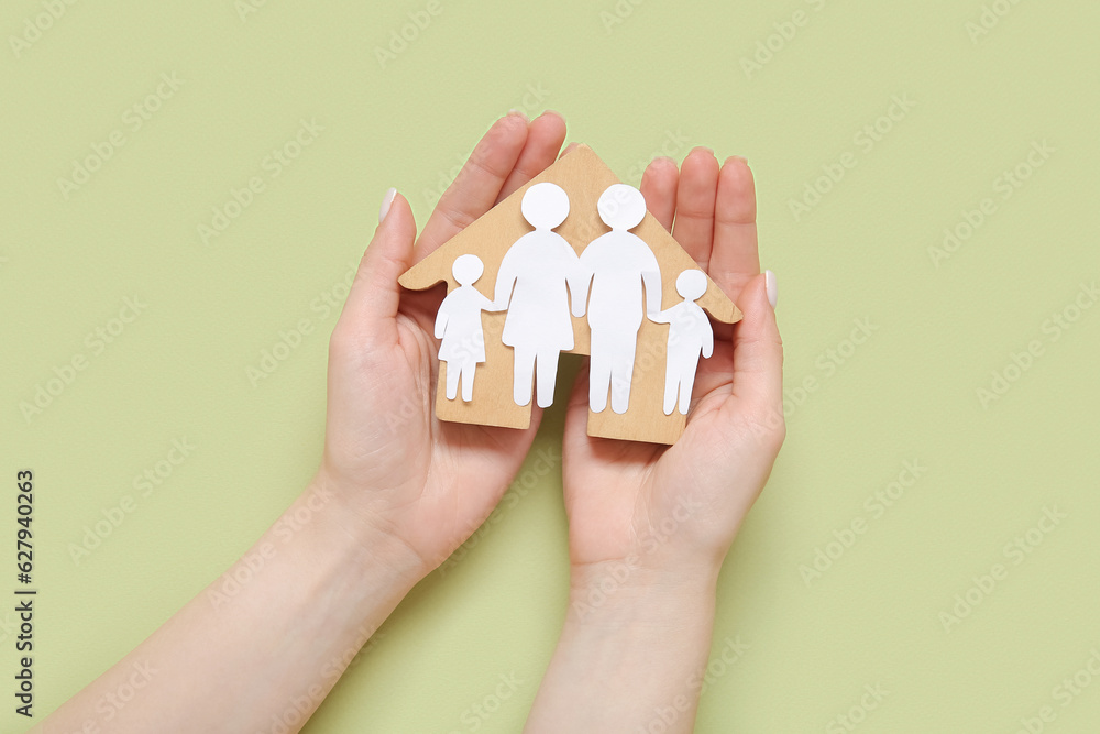 Woman holding figures of family and wooden house on green background