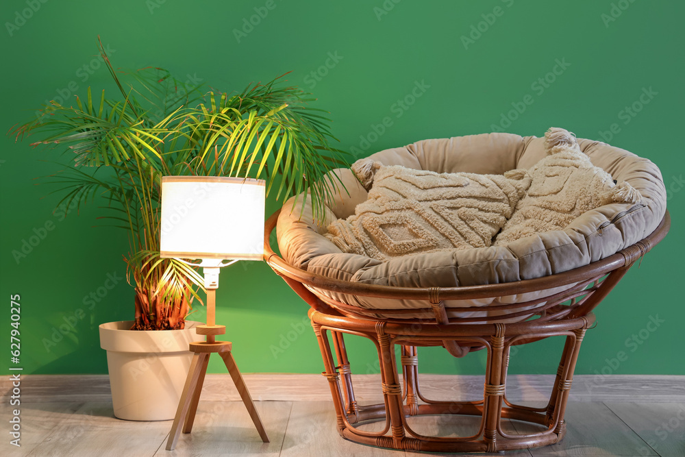 Glowing lamp with armchair and palm tree near green wall in room