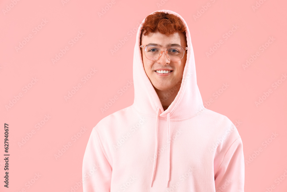 Young redhead man in hoodie on pink background, closeup