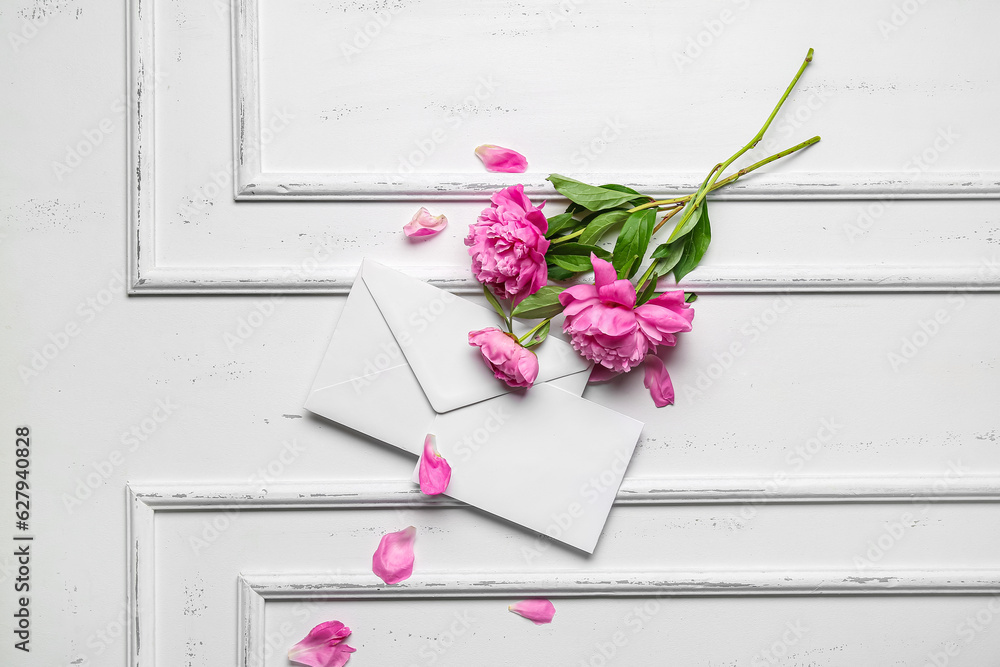 Composition with blank card, envelope and beautiful peony flowers on light background