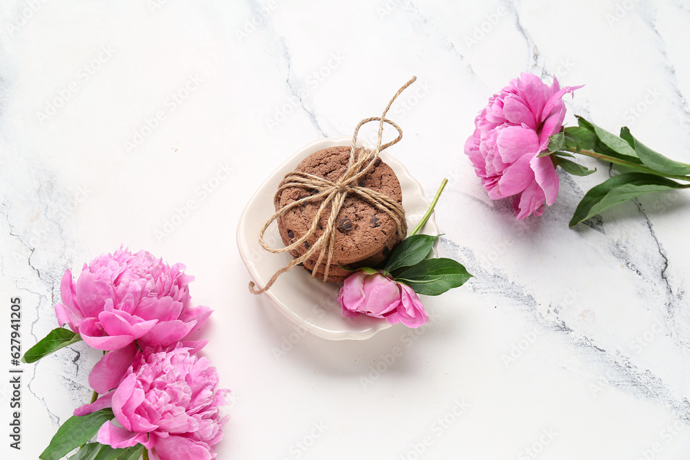 Plate with sweet cookies and beautiful peony flowers on light background