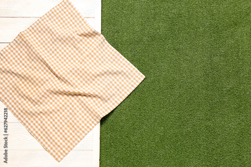 Clean napkin on light wooden table against green grass background