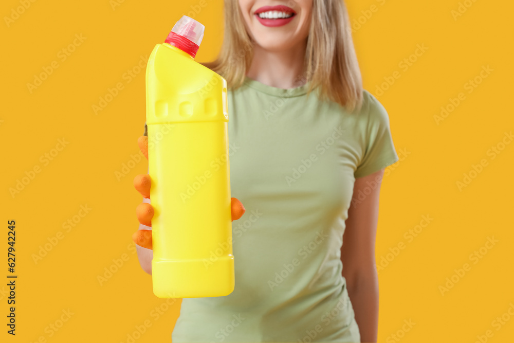 Young woman with bottle of detergent on orange background, closeup