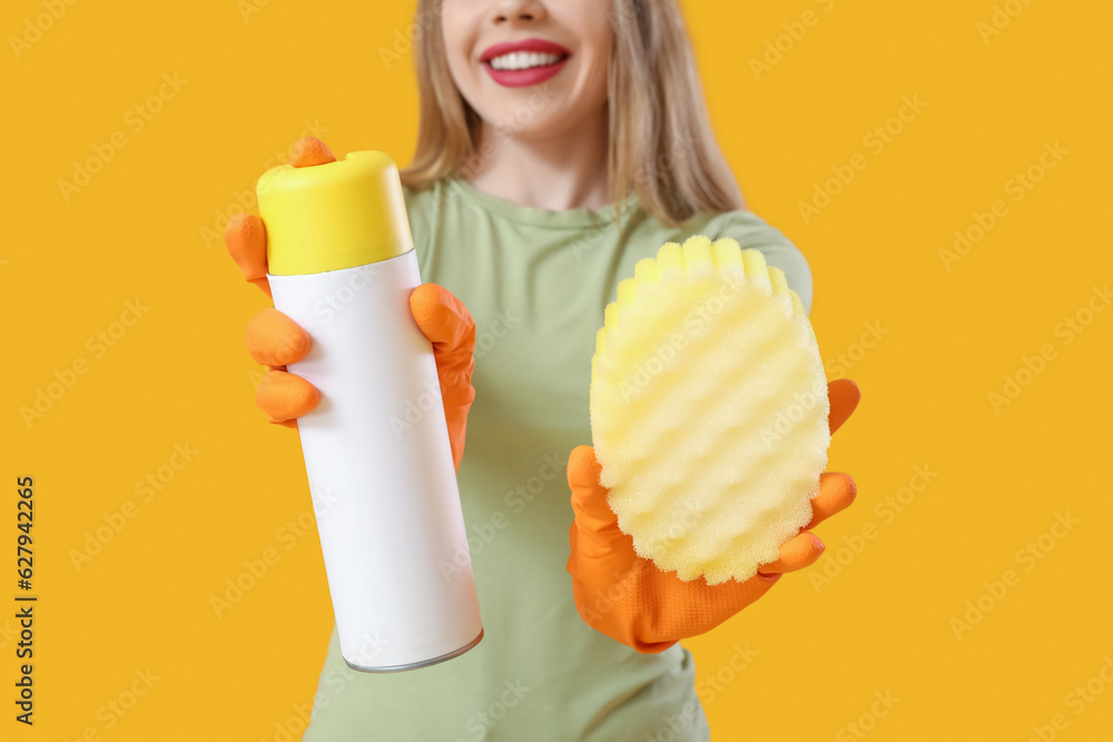 Young woman with air freshener and cleaning sponge on orange background