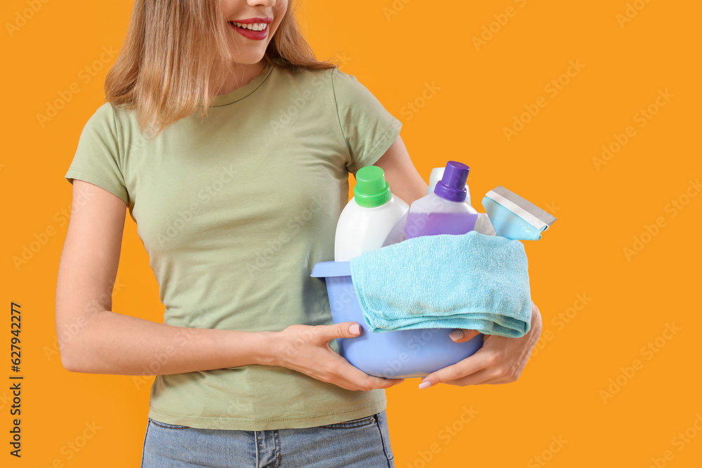 Young woman with cleaning supplies on orange background, closeup