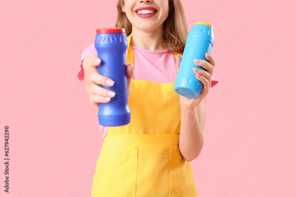 Young woman with bottles of detergent on pink background, closeup