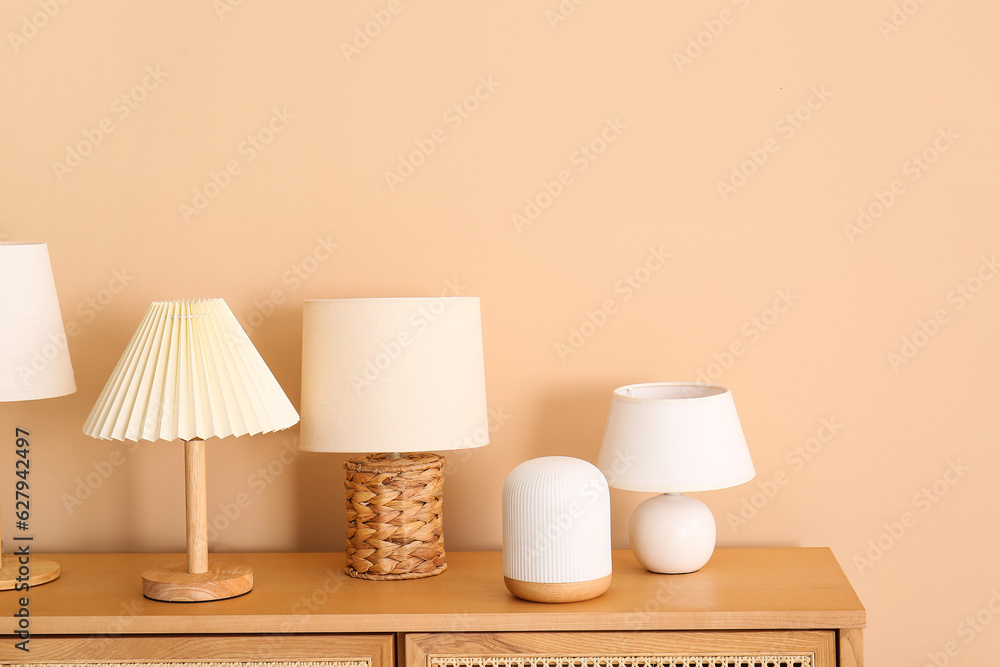 Set of different table lamps on wooden cabinet near beige wall