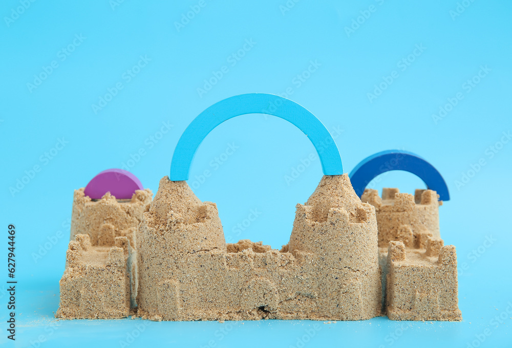 Castle made of sand with beach toys on blue background