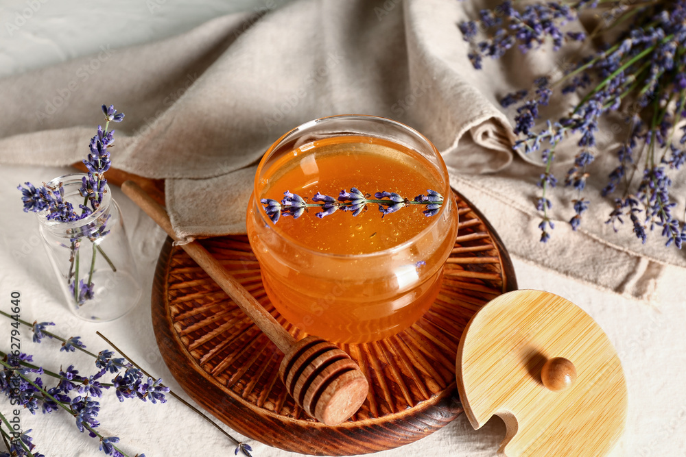 Wooden board with jar of sweet lavender honey, dipper and flowers on white table