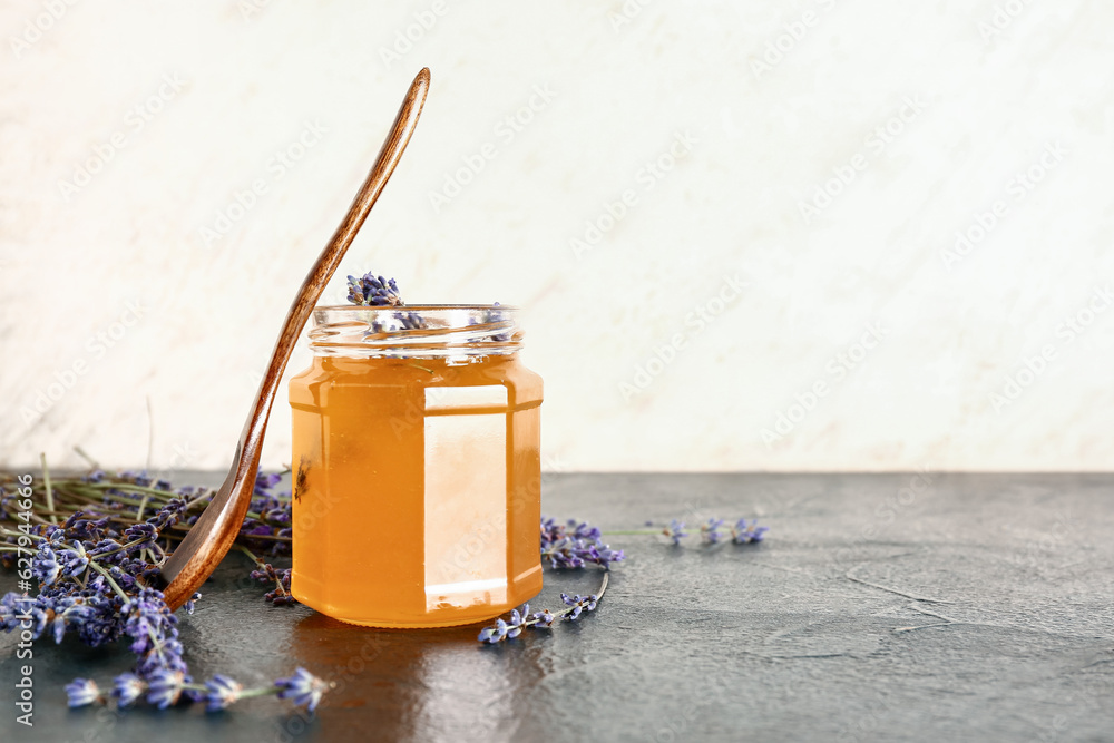 Jar of sweet lavender honey and flowers on dark table