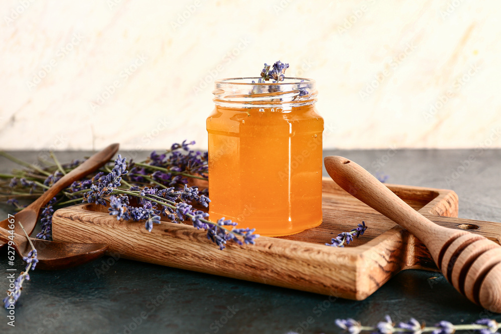 Wooden board with jar of sweet lavender honey, dipper and flowers on dark table