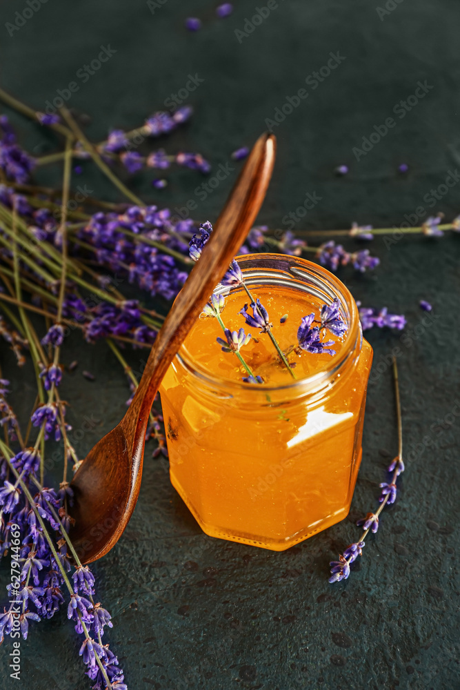 Jar of sweet lavender honey and flowers on dark table