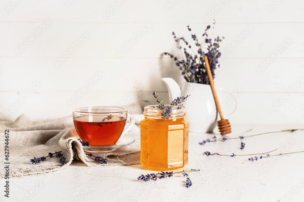 Jar with sweet lavender honey and cup of tea on white background