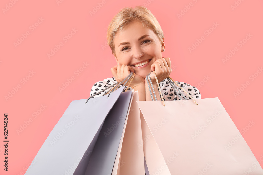 Happy beautiful young woman with shopping bags on pink background