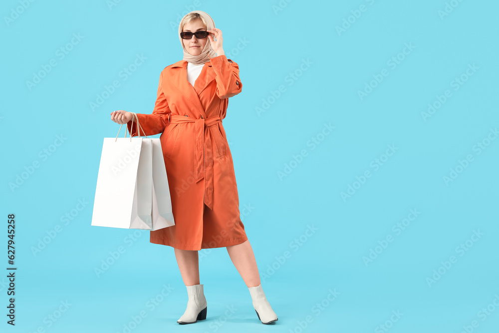 Stylish beautiful young woman with shopping bags on blue background