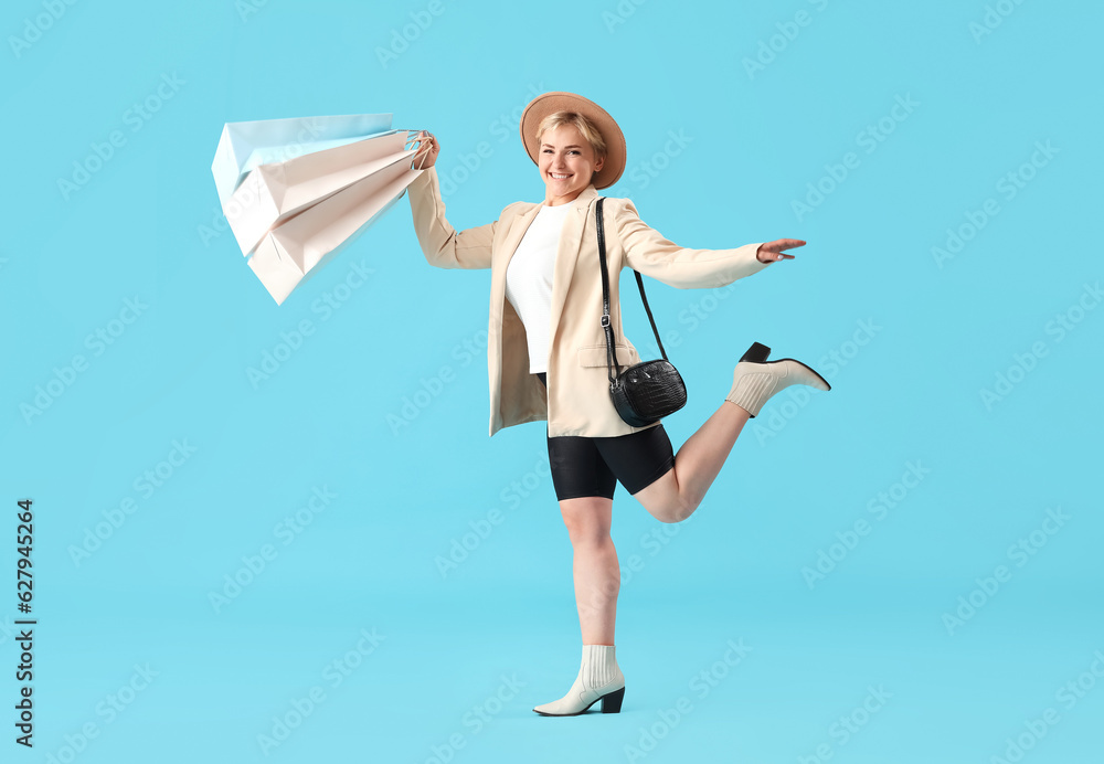 Happy beautiful young woman with shopping bags on blue background