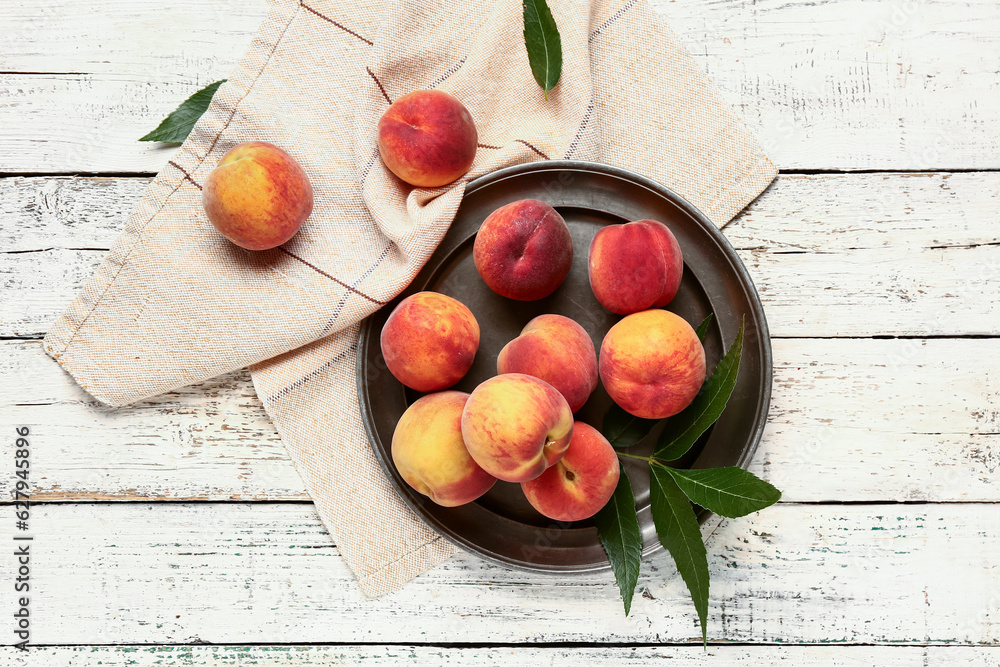 Plate with sweet peaches and leaves on white wooden background