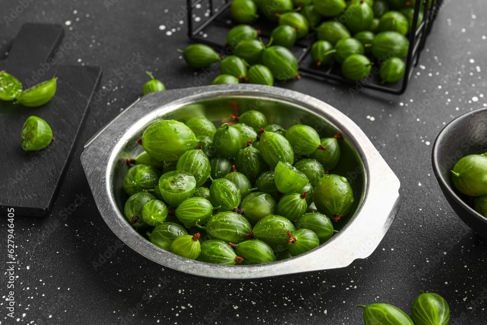 Metal plate with fresh gooseberries on black background